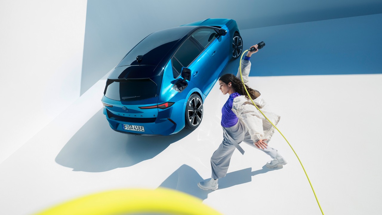 Top view of a blue Opel Astra Electric with a black roof with woman twirling a yellow charging cable